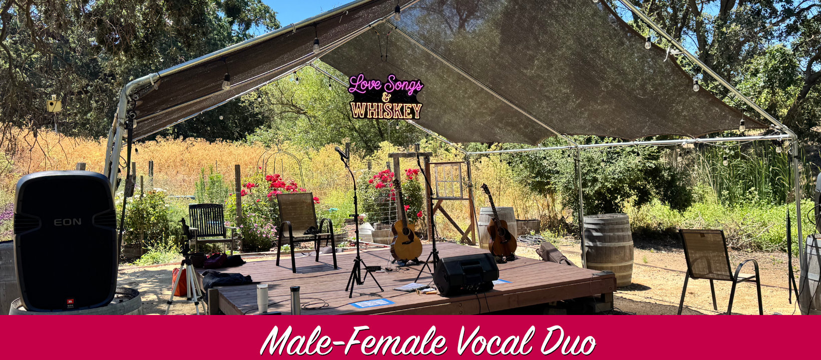 A beautiful outdoor stage with guitars and microphone surrounded by flowers and oak trees with a neon sign declaring Love Songs and Whiskey will be playing