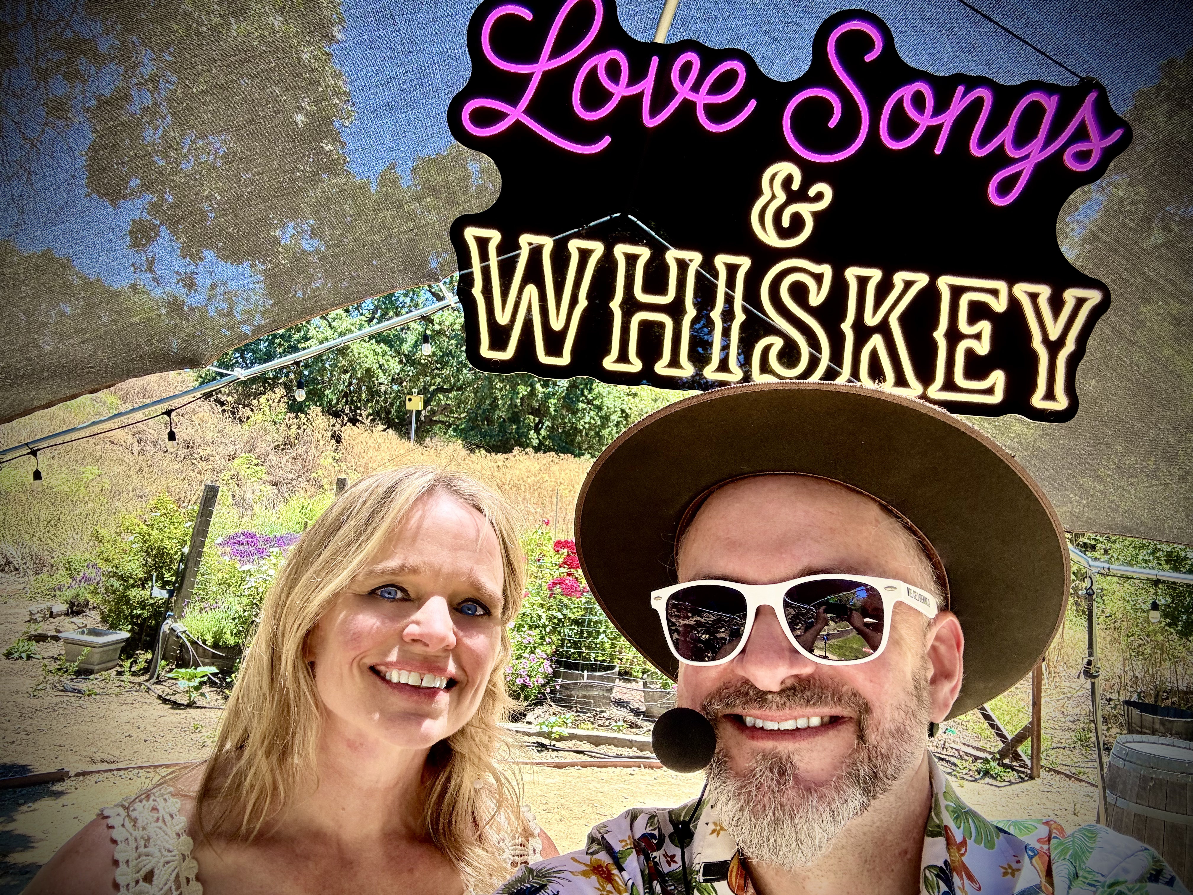 Love Songs & Whiskey smile in front of a garden with a neon sign of the band's name overhead